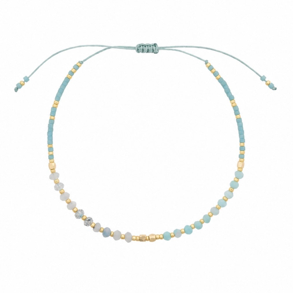 A delicate beaded necklace with a light blue cord, featuring pale blue and white beads accented with small gold spacer beads, displayed on a clean white background.