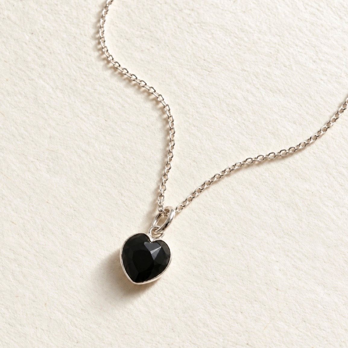 A delicate silver chain necklace with a small black onyx heart-shaped pendant