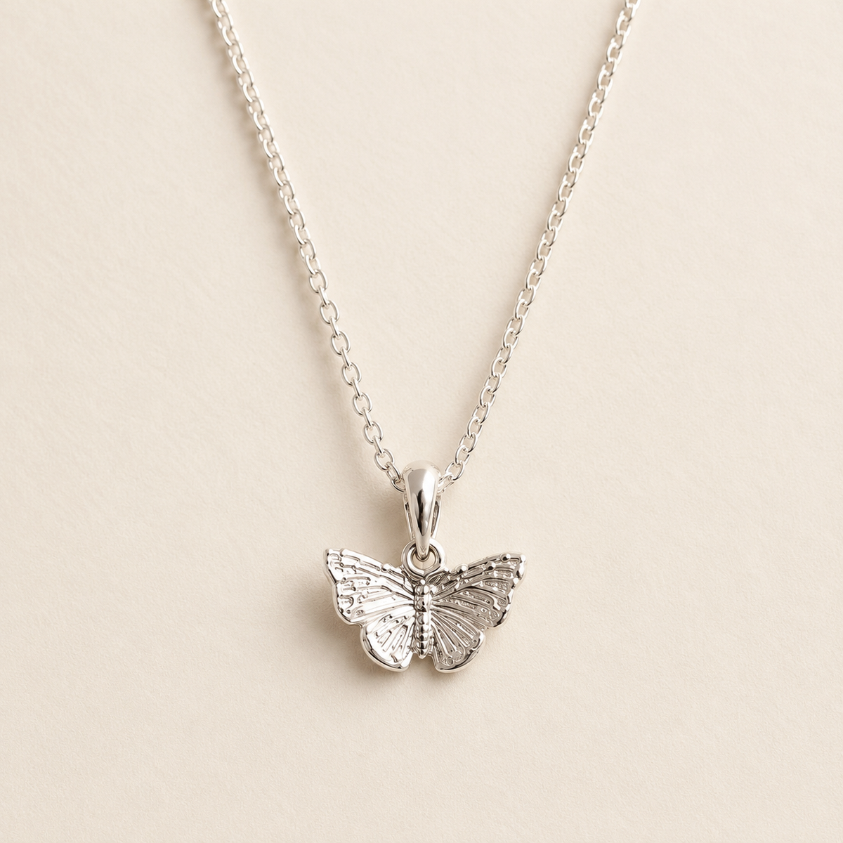 A silver butterfly pendant necklace on a delicate silver chain, displayed against a light beige background.