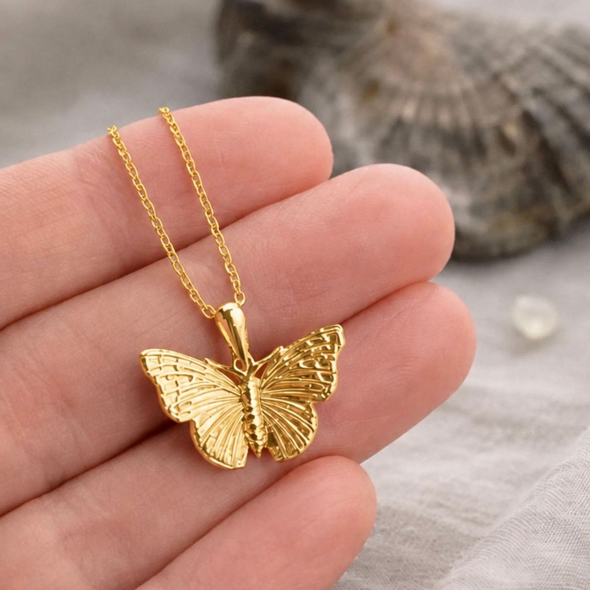 A gold butterfly pendant necklace with a textured wing design held in hand to show scale