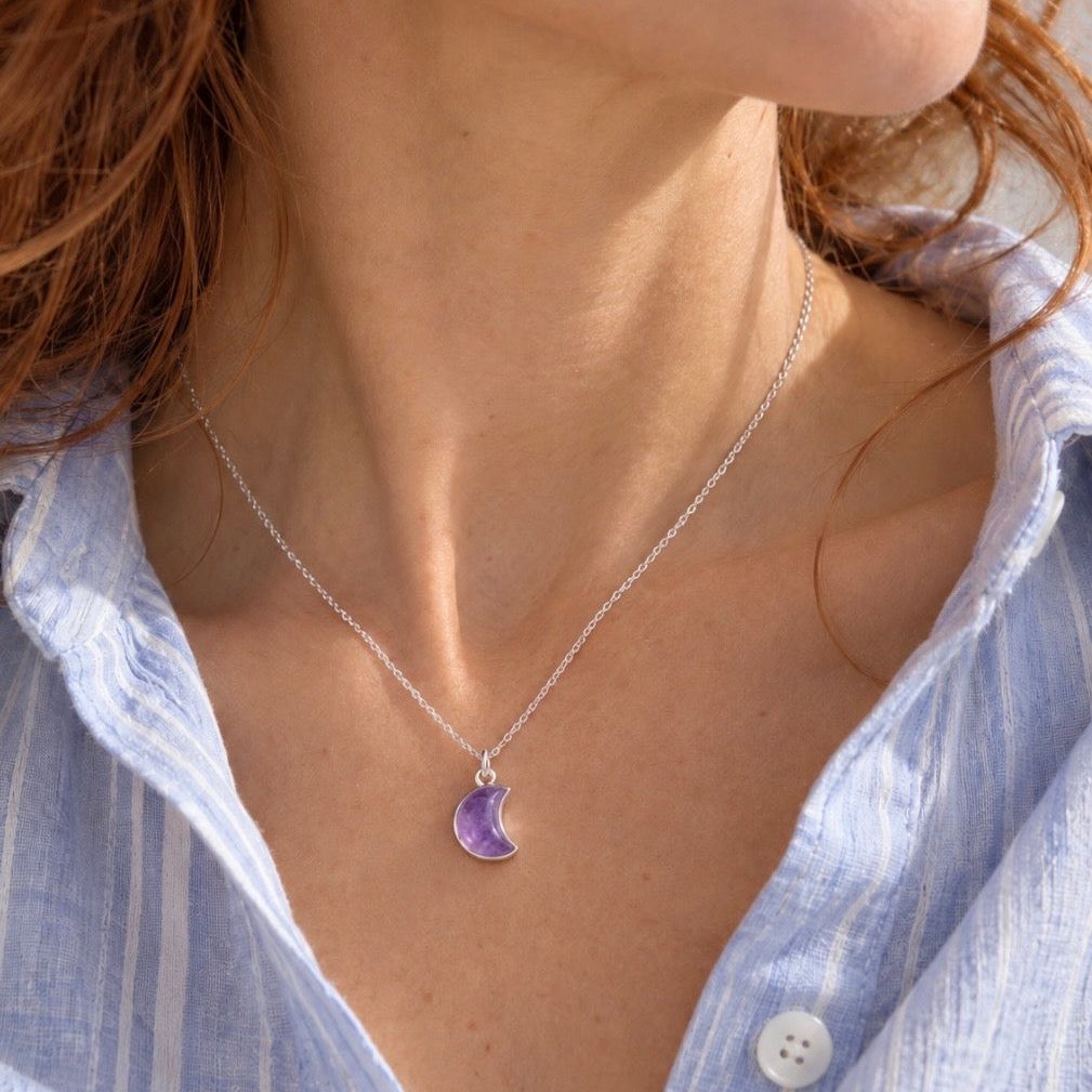 A silver crescent moon pendant necklace with a polished purple amethyst stone, displayed on model