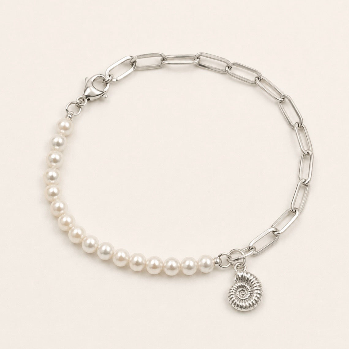 A silver chain bracelet featuring a section of white freshwater pearls and a small silver ammonite fossil  charm, displayed on a light cream background.