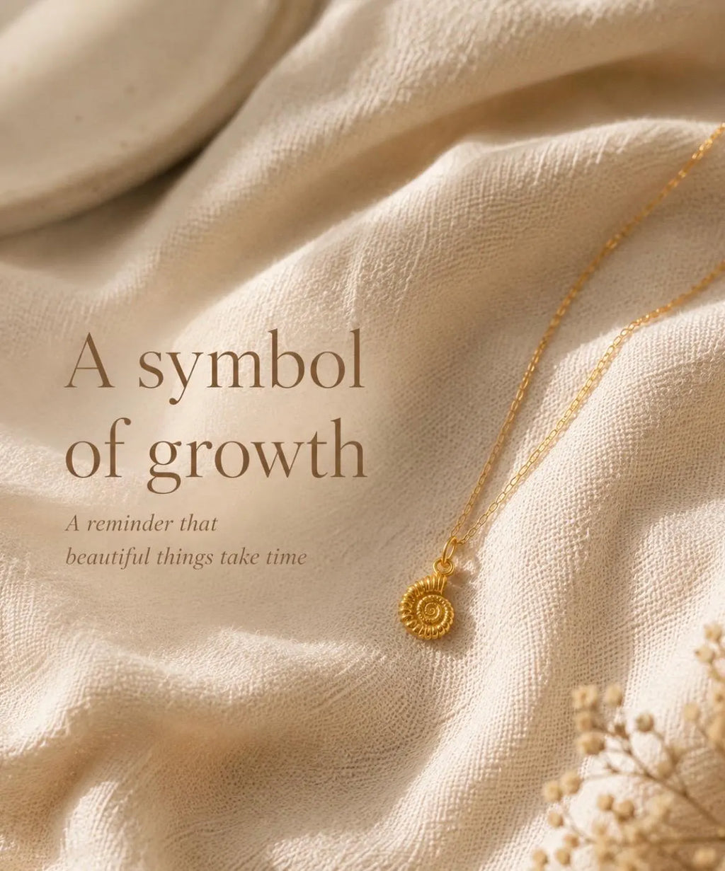 A gold spiral pendant necklace on a delicate chain, displayed on draped beige linen fabric with decorative dried flowers. Text on the left reads, 'A symbol of growth A reminder that beautiful things take time.