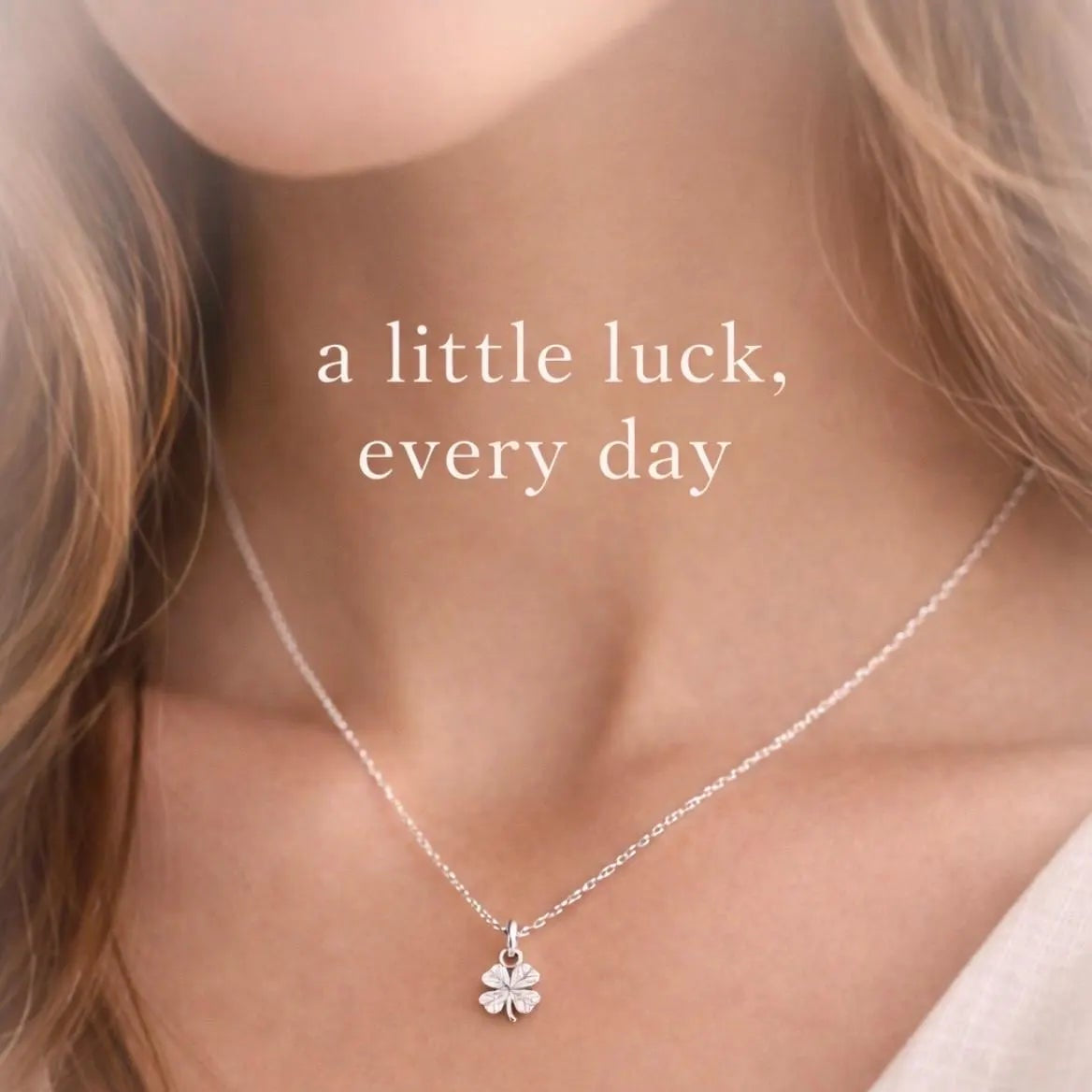 A close-up lifestyle shot of a woman wearing a delicate silver chain necklace with a small silver four-leaf clover pendant. 
