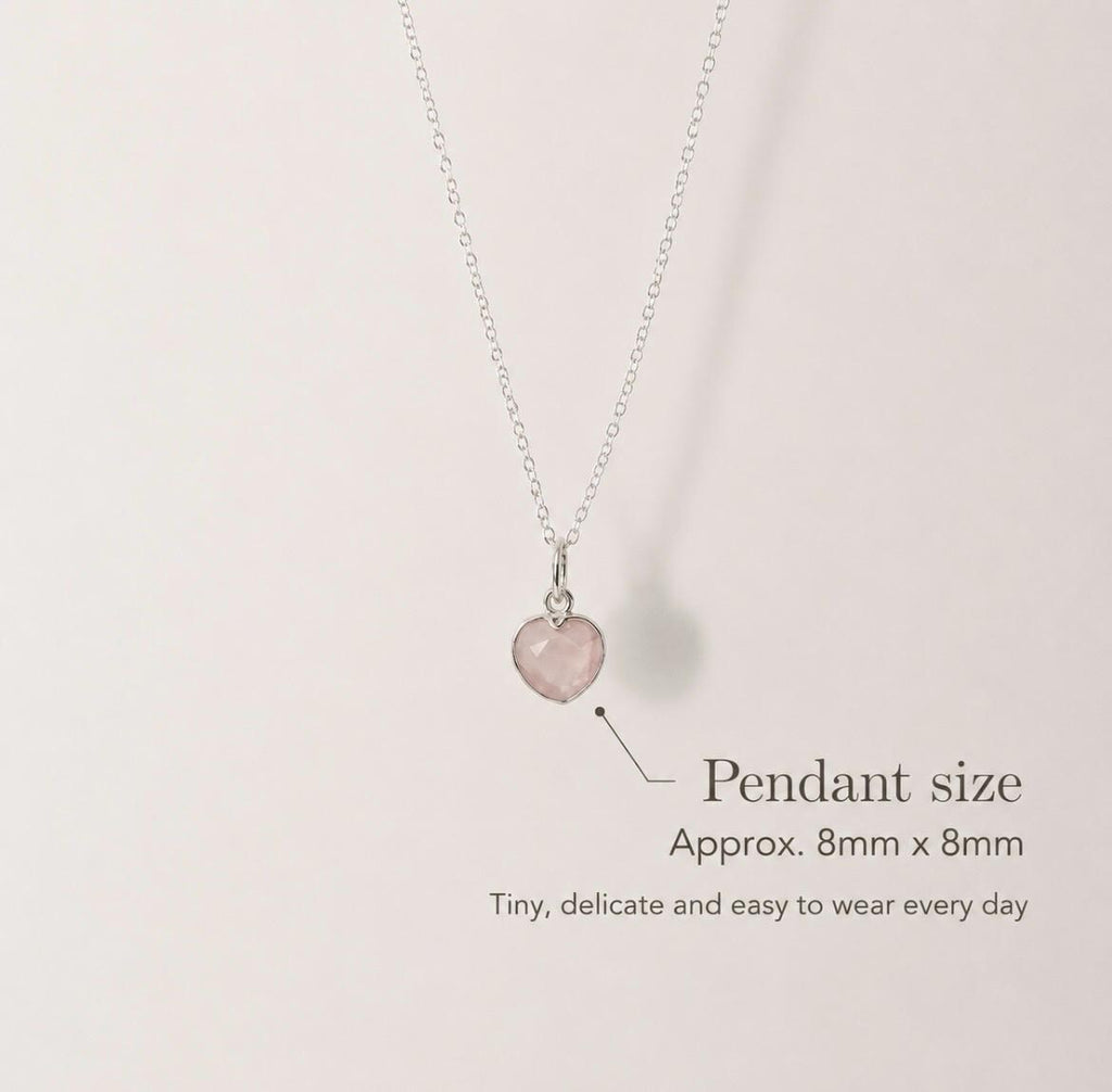 A delicate silver necklace with a small, pale pink heart-shaped pendant, shown against a light beige background with text indicating the pendant size is approximately 8mm x 8mm.
