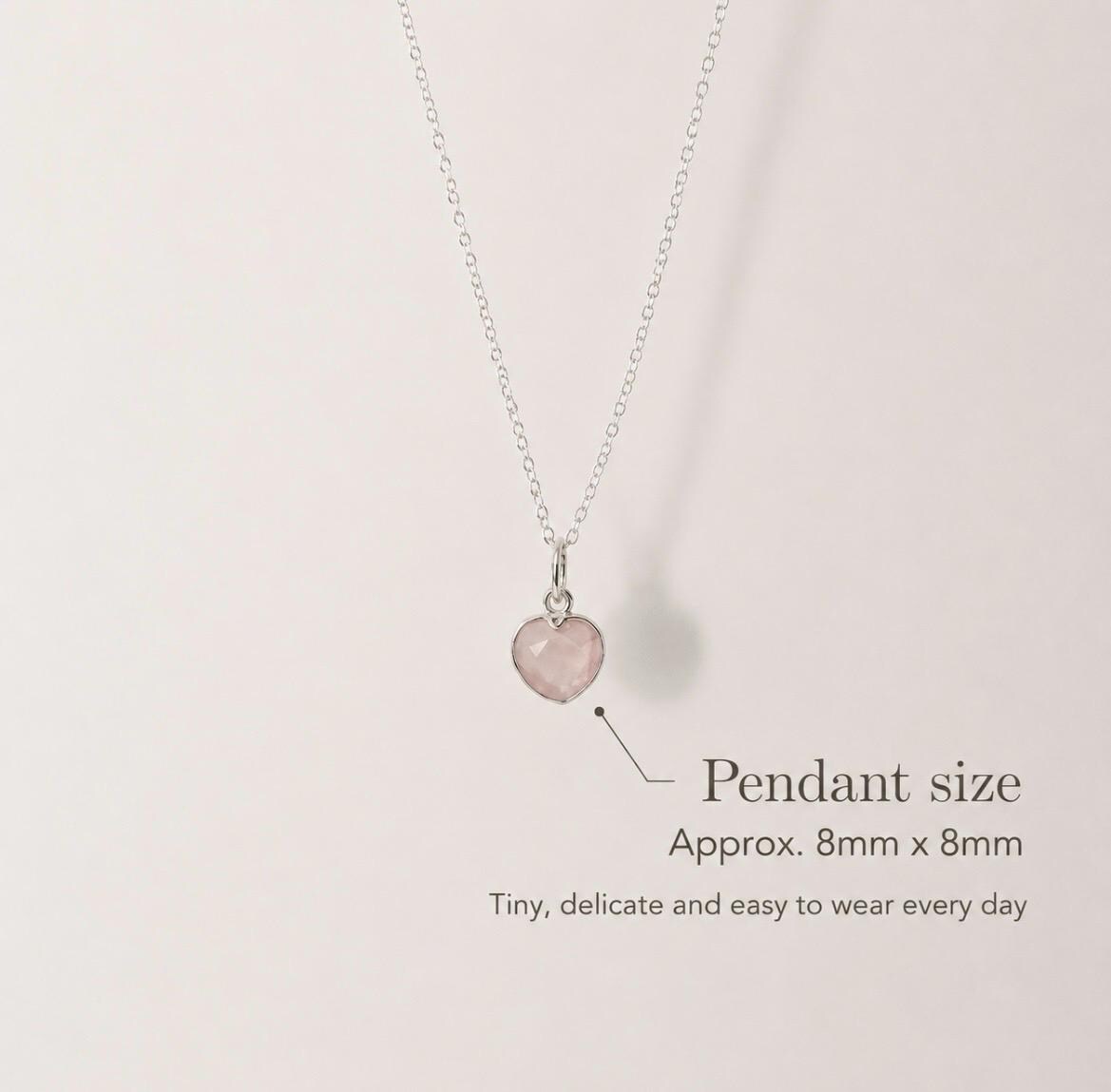 A delicate silver necklace with a small, pale pink heart-shaped pendant, shown against a light beige background with text indicating the pendant size is approximately 8mm x 8mm.