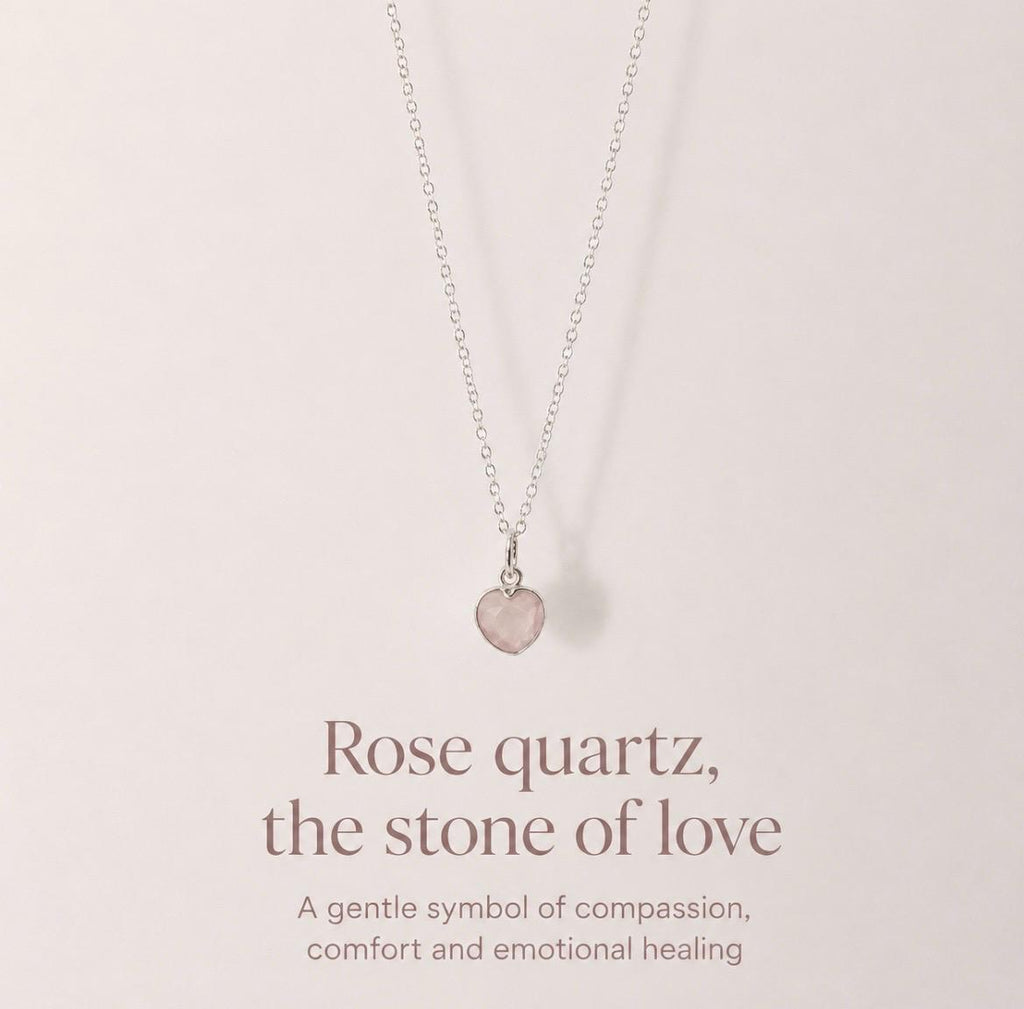 A delicate silver necklace with a small rose quartz heart pendant, displayed against a soft beige background with elegant text below reading 'Rose quartz, the stone of love'.
