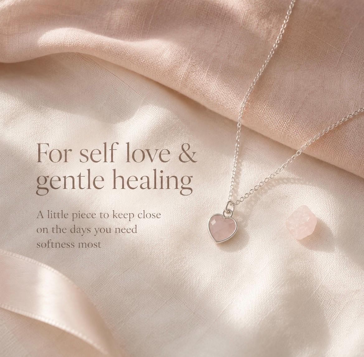 A delicate silver necklace with a small pink rose quartz heart pendant, displayed on soft draped satin fabric with elegant text on the left side.