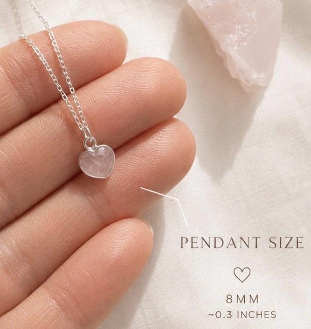 A silver chain necklace with a small heart-shaped pendant made of rose quartz stone, held on a person's fingers. Text on the image indicates the pendant size is 8 mm (~0.