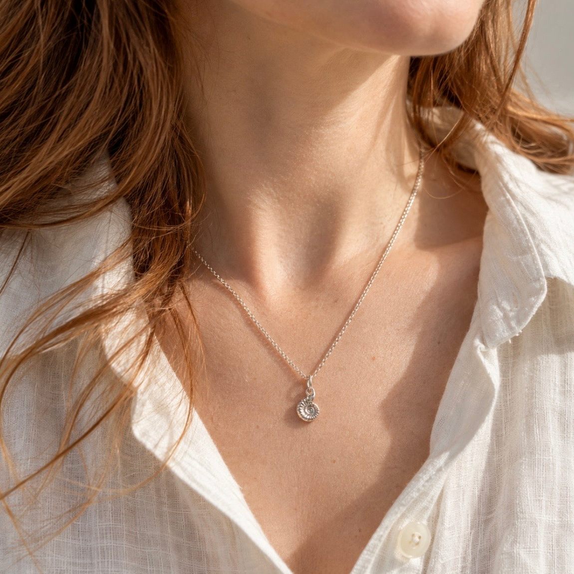 Small sterling silver ammonite necklace worn with a white linen shirt, showing the delicate pendant at its natural scale, 