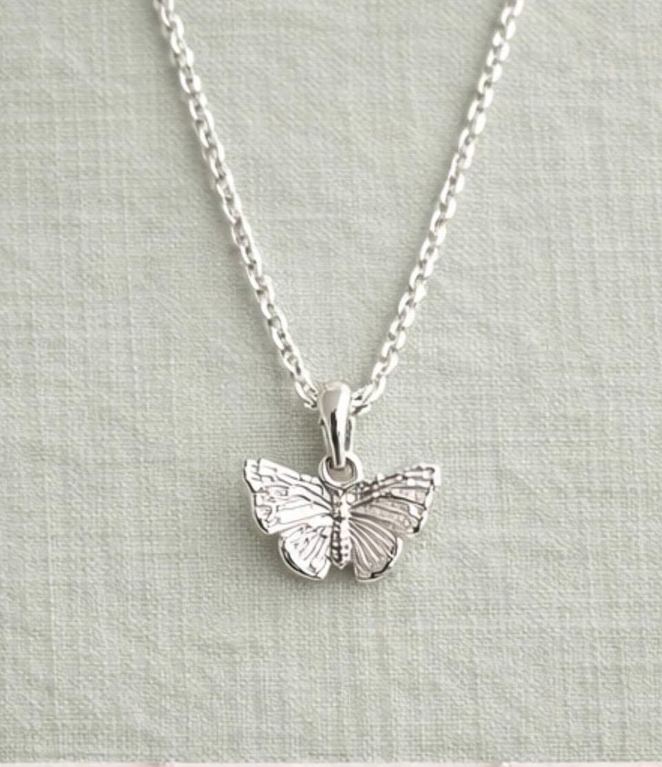 A silver butterfly pendant necklace on a delicate silver chain, displayed against a textured light gray fabric background.