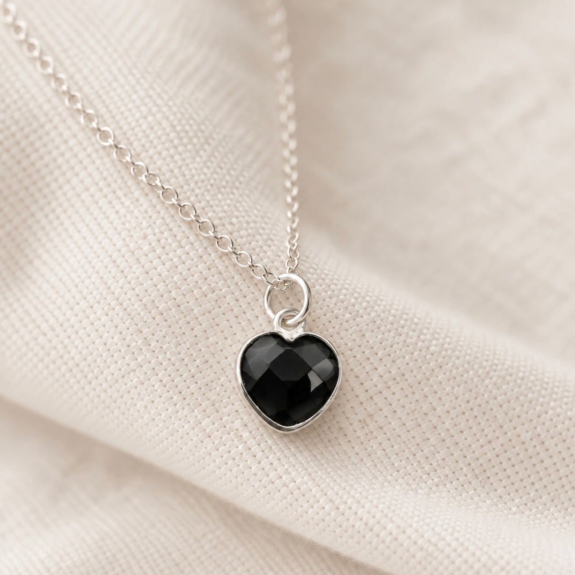 delicate silver chain necklace with a small black onyx heart-shaped pendant on a cream textile background